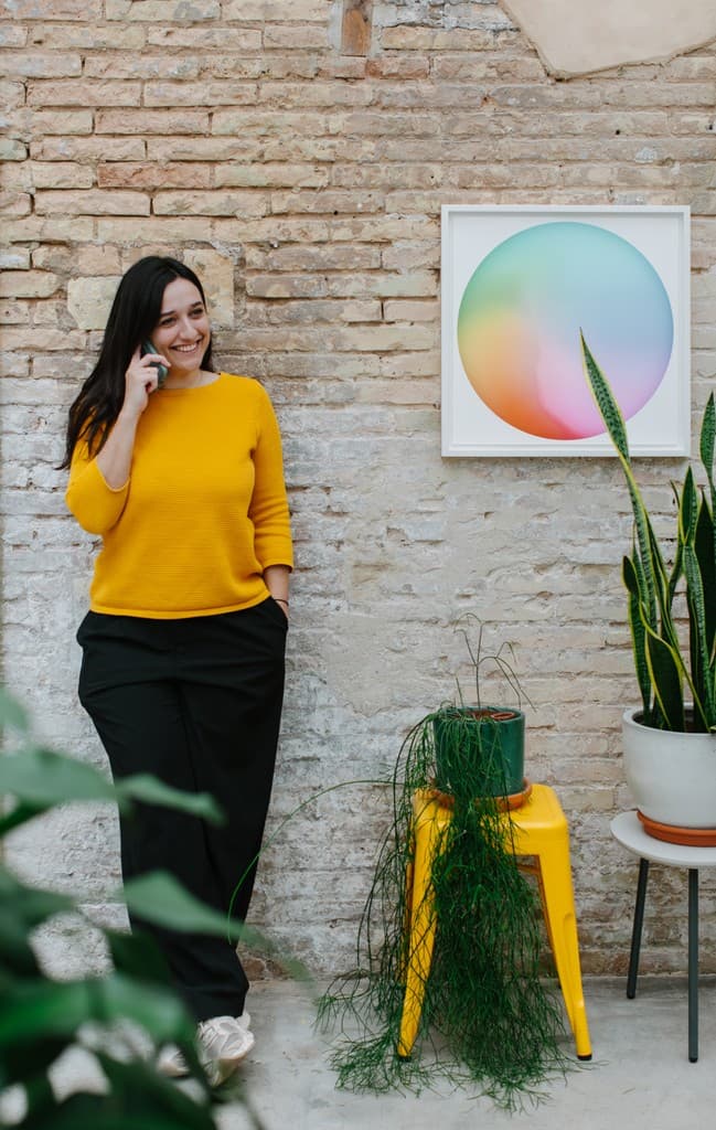 A team member standing in the studio next to a plant and a colourful artwork.
